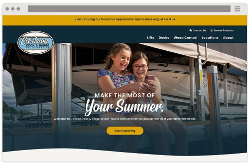 Two smiling girls sit on a dock in front of boats, looking at a smartphone. The website banner reads 