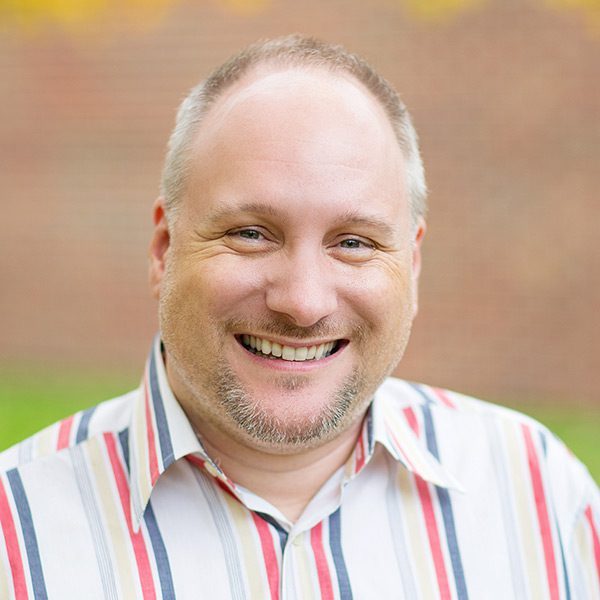 Smiling man in a striped shirt stands confidently, demonstrating trust, against a blurred background—perfect for conveying authenticity in online reviews or on a website.