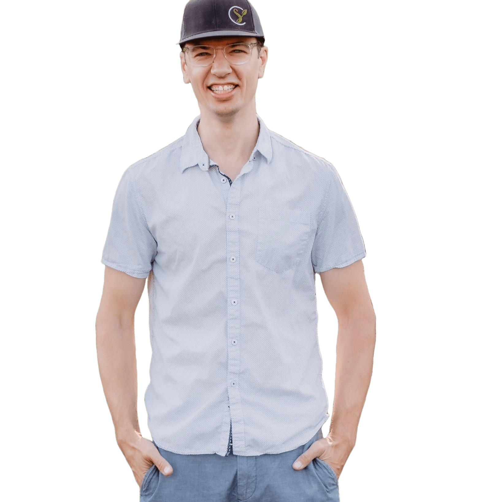 A person wearing a light blue short-sleeve button-up shirt, blue pants, and a black cap smiles with hands in pockets against a plain background, embodying marketing success.